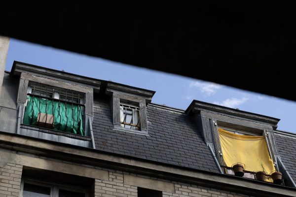Dachgeschoss eines Pariser Wohngebäudes, an einigen Fenstern hängen Tücher als improvisierter Sonnenschutz