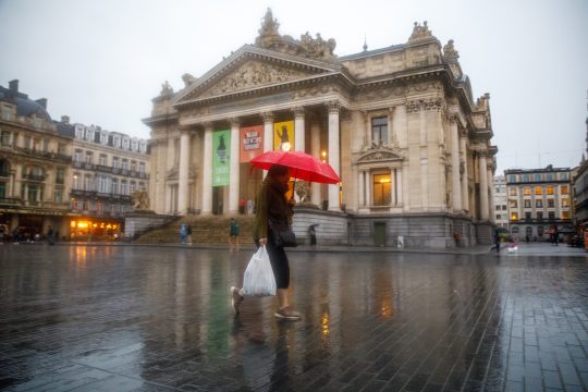 Ein Passant mit rotem Schirm geht im Regen an der Brüsseler Börse vorbei