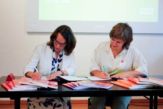 Die Leiterin des Goethe-Instituts in Brüssel, Julia Sattler, und die Vizerektorin der Universität Antwerpen, Chris Van Ginneken, unterzeichnen Dokumente