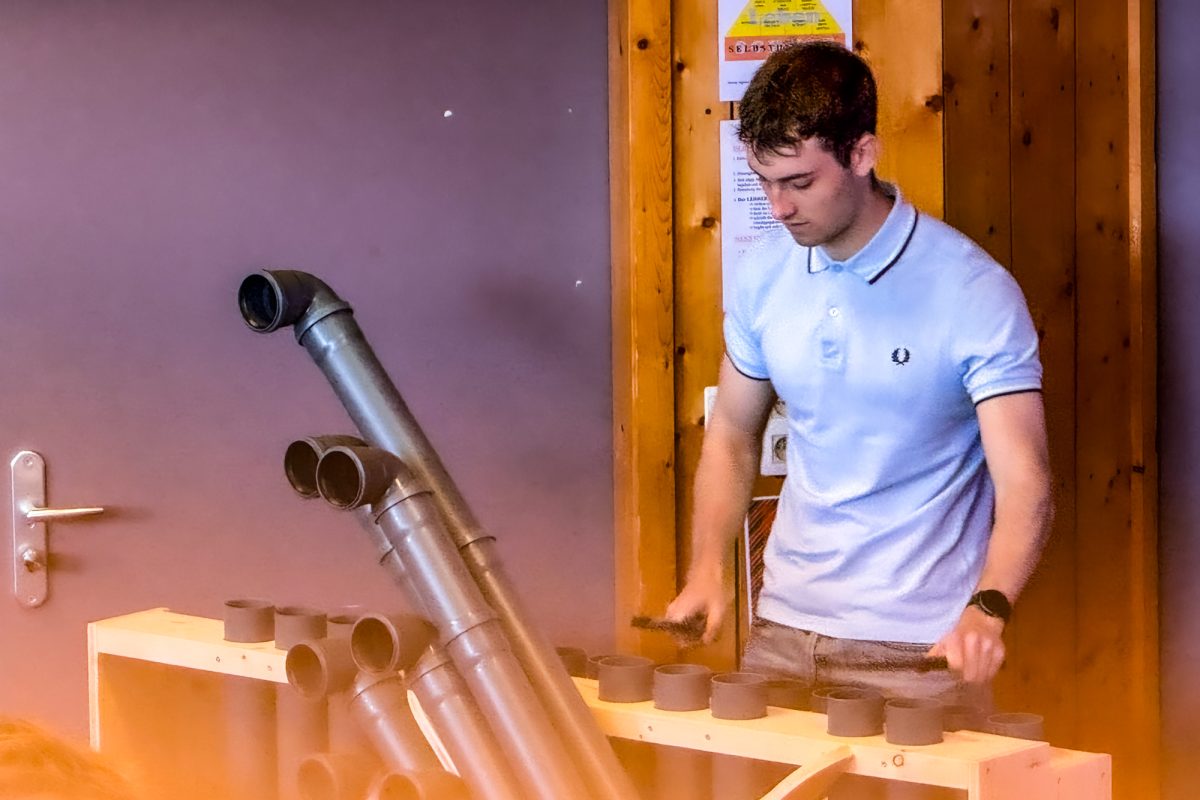 Junger Mann spielt auf einem selbstgebauten Instrument mit mehreren Röhren, das von der Optik her wie eine Mischung aus Xylophon und Orgel aussieht