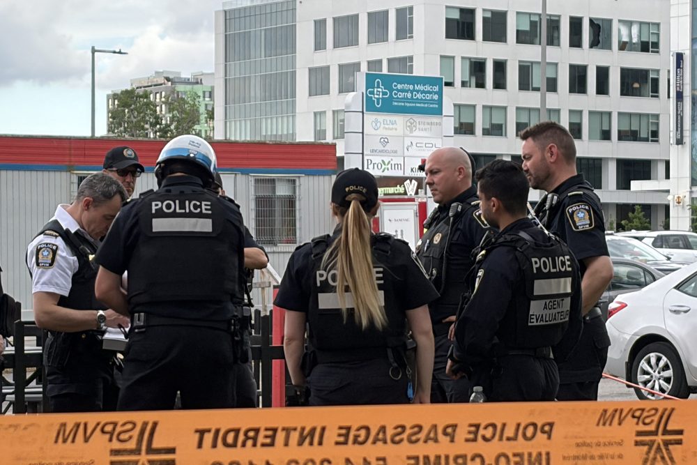 In der Ferne sind beschädigte Fenster zu sehen (oben rechts), während sich die Polizei in der Nähe des Tatorts einer Schießerei in Montreal versammelt
