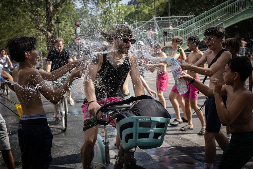 Ein Mann fährt Fahrrad, eine Gruppe Teenager bespritzt ihn mit Wasser