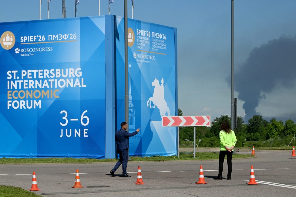 Banner mit dem Hinweis auf das Wirtschaftsforum in St. Peterburg und im Hintergrund eine Rauchsäule nach ukrainischen Angriffen