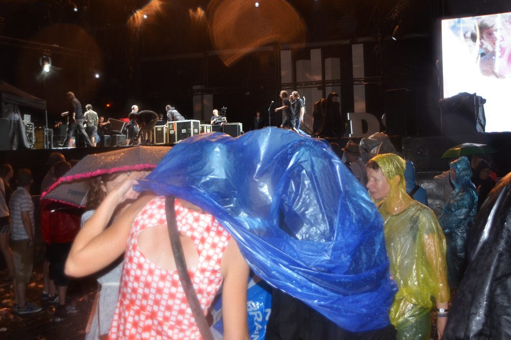 Festivalbesucher versuchen sich mit Regenponcho und Plastikfolie vor einem Wolkenbruch zu schützen