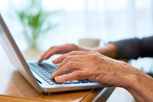 Hand von älterem Menschen an Tastatur von Laptop