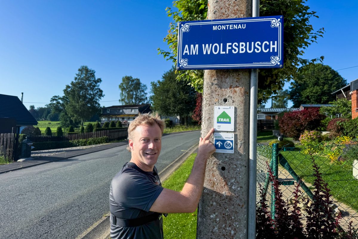 Daniel Baltus zeigt auf ein Hinweisschild auf die Trailrunning-Strecke in der Straße "Am Wolfsbusch"