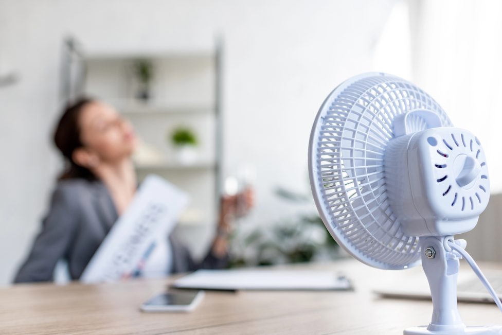 Frau kühlt sich vor einem Ventilator ab