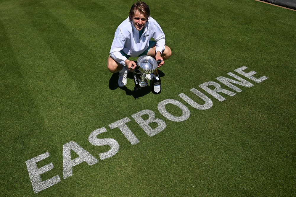 Zizou Bergs hält den Siegerpokal in den Händen, er steht auf dem Tennisrasen, auf dem das Wort "Eastbourne" geschrieben wurde