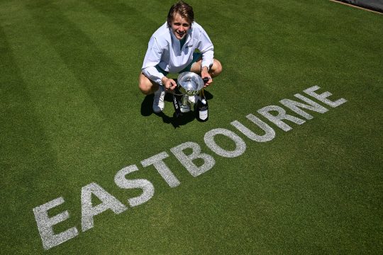 Zizou Bergs hält den Siegerpokal in den Händen, er steht auf dem Tennisrasen, auf dem das Wort "Eastbourne" geschrieben wurde