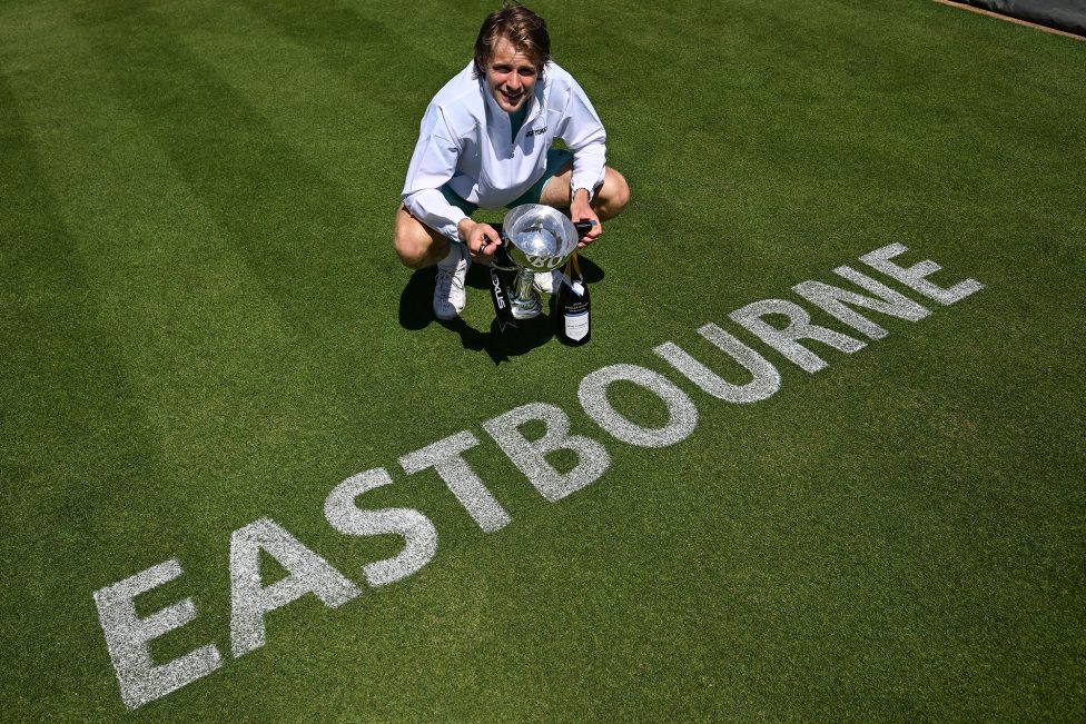 Zizou Bergs hält den Siegerpokal in den Händen, er steht auf dem Tennisrasen, auf dem das Wort "Eastbourne" geschrieben wurde