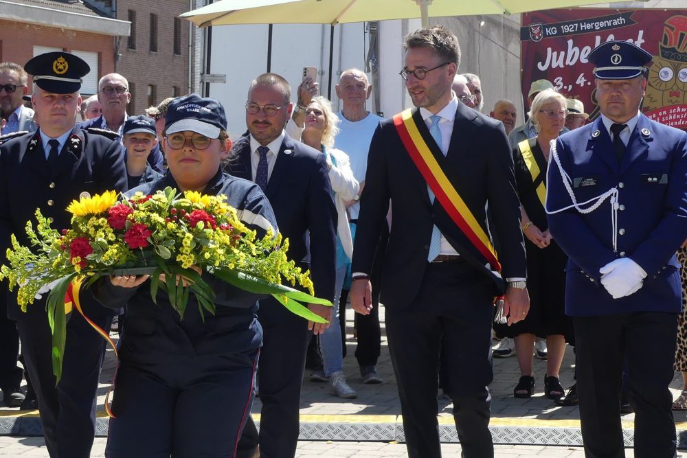 Bürgermeister Hilligsmann mit Scherpe in Nationalfarben, dazu Armeevertreter, eine Frau trägt ein Blumengedeck