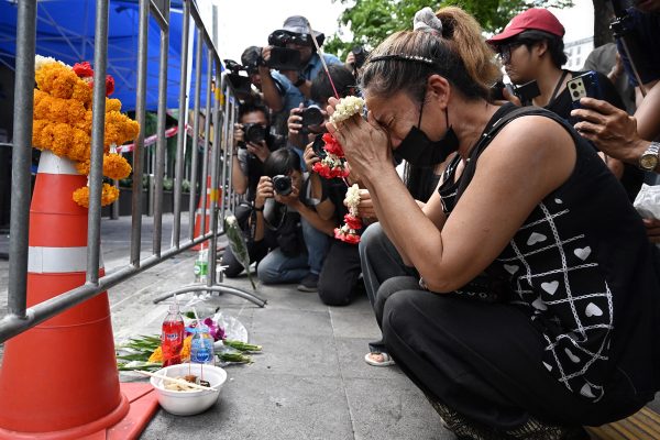 Eine Frau hält Räucherstäbchen und Blumen und kniet betend vor der Bar