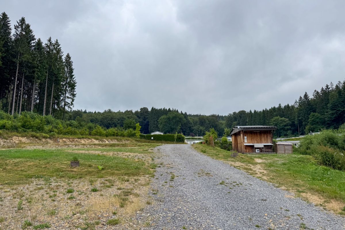 Schotterweg auf dem Camping, neben dem eine Holzhütte steht