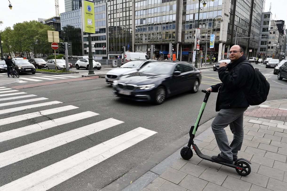 Mann mit E-Roller steht an Zebrastreifen in Brüssel