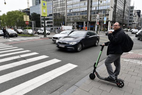 Mann mit E-Roller steht an Zebrastreifen in Brüssel