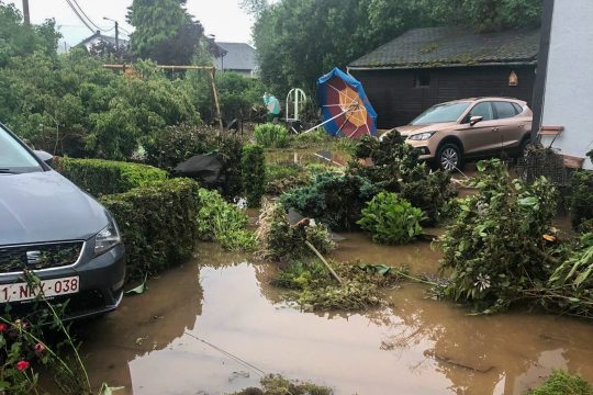 Der Garten steht unter Wasser, im Hintergrund ein Auto und ein weggeschwemmter Sonnenschirm