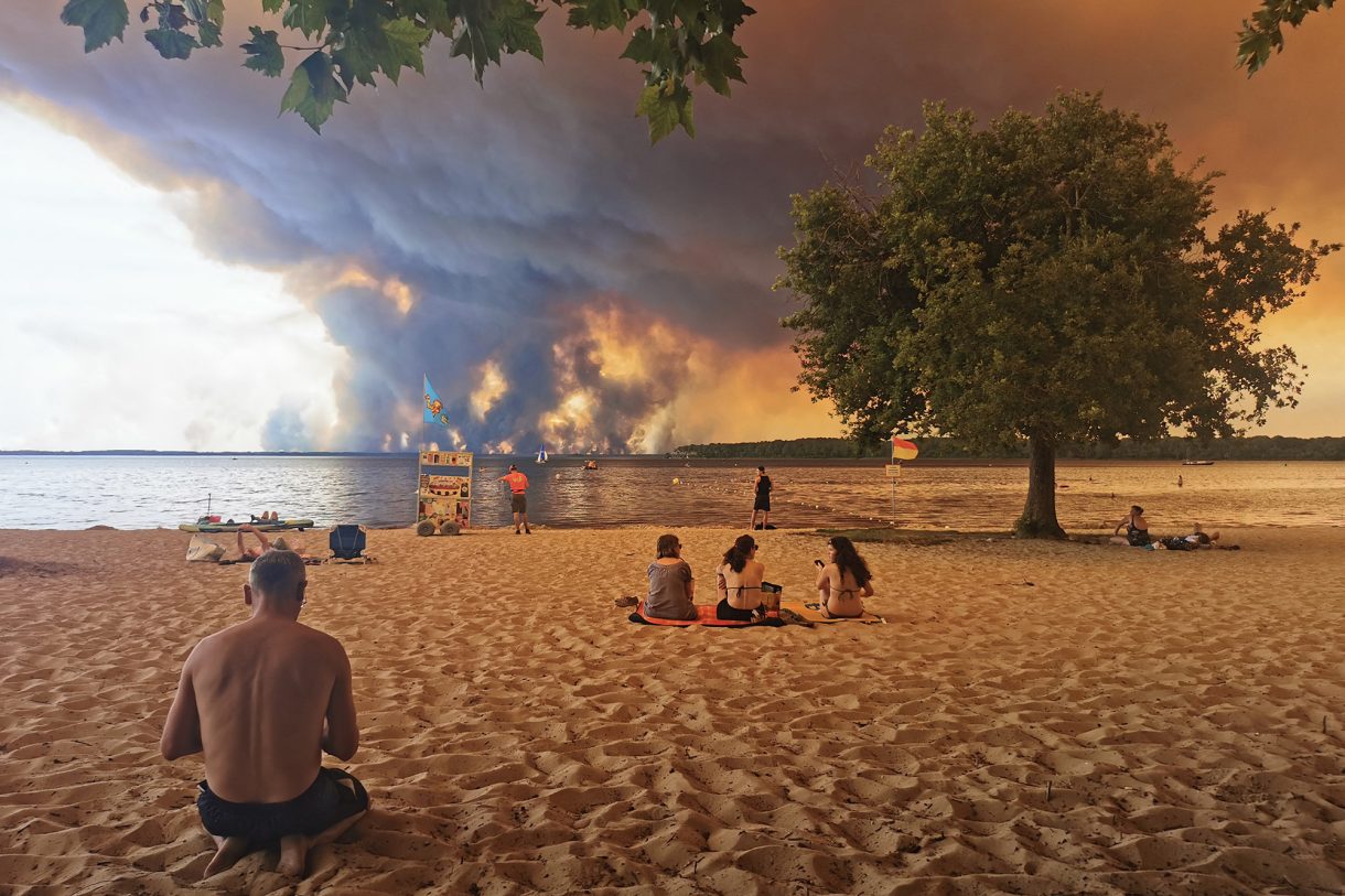 Strandbesucher in Lacanau im Südwesten Frankreichs - im Hintergrund wütet ein Waldbrand