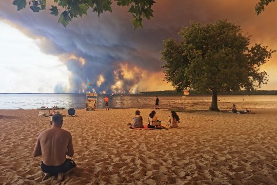 Strandbesucher in Lacanau im Südwesten Frankreichs - im Hintergrund wütet ein Waldbrand