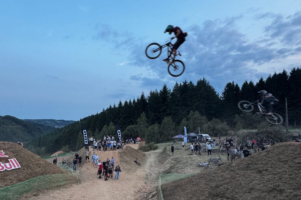 Zwei Freerider springen durch die Luft, von unten schauen Menschen hoch