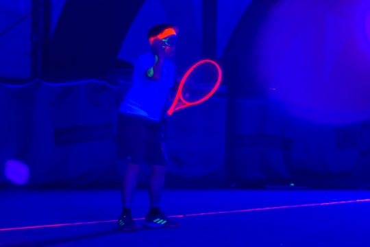 Ein Spieler auf dem Feld - im Schwarzlicht leuchten sein Schläger und sein Stirnband rot