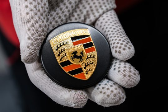 Nahansicht von Hand in Handschuh, die ein Porsche-Emblem hält