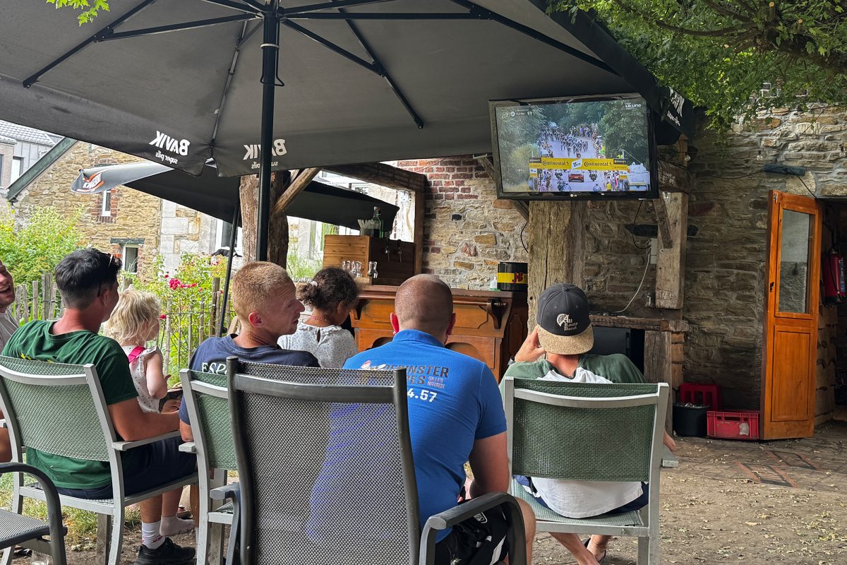 Besucher des Lokals schauen gemeinsam auf der Terrasse ein Radrennen, das auf einem Fernseher gezeigt wird