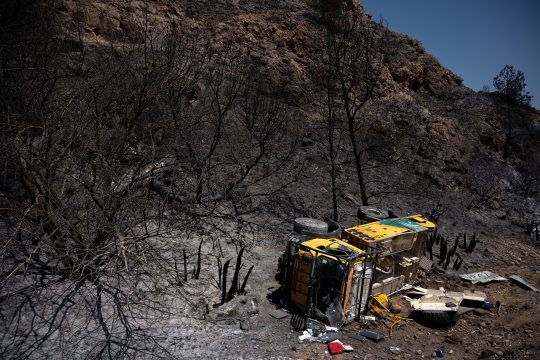 ein gelber LKW der andalusischen Feuerwehr liegt auf der Seite in einem Abhang, drumherum verbrannte Vegetation