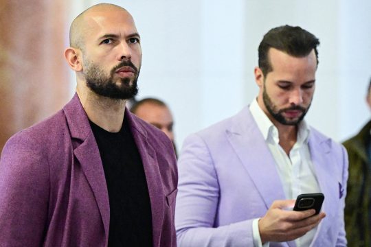 Bildaufnahme von Andrew und Tristan Tate, bei der Letztgenannter auf sein Handy blickt