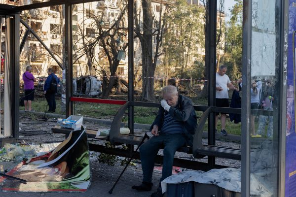 Ein Mann mit einem bandagierten Arm sitzt an einer beschädigten Bushaltestelle in der Nähe eines Wohnhauses, das bei einem russischen Luftangriff auf die ukrainische Hauptstadt Kiew am 2. Juli beschädigt wurde.