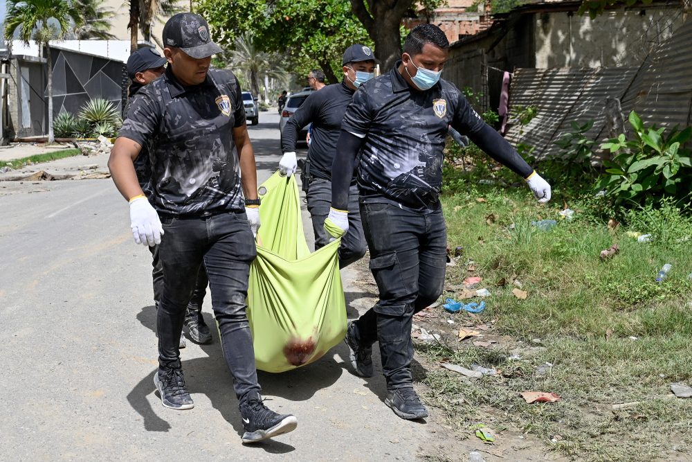 venezolanische Polizisten tragen eine mit einem grünen Tuch bedeckte Leiche eine Straße entlang