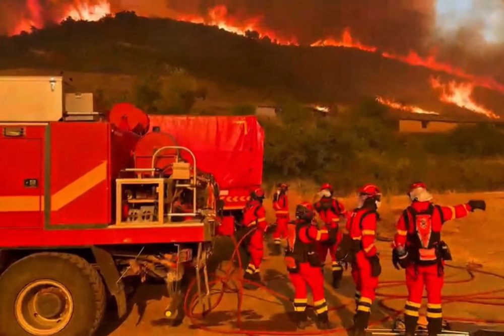 Mitglieder der spanischen Militäreinheit für Notfälle neben einem Einsatzfahrzeug, im Hintergrund ein Hügel mit einem lodernden Feuer
