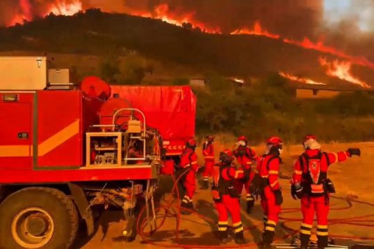 Mitglieder der spanischen Militäreinheit für Notfälle neben einem Einsatzfahrzeug, im Hintergrund ein Hügel mit einem lodernden Feuer
