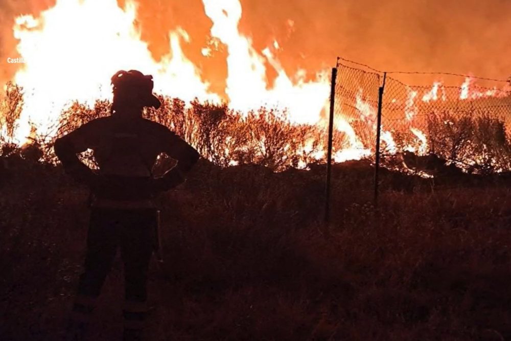 Lodernde Flammen bei Nacht beim Waldbrand in Castilla-La-Mancha, davor steht ein Feuerwehrmann
