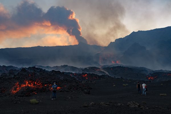 Menschen betrachten Lavaströme am Ätna, im Hintergrund sind große Rauchwolken zu sehen