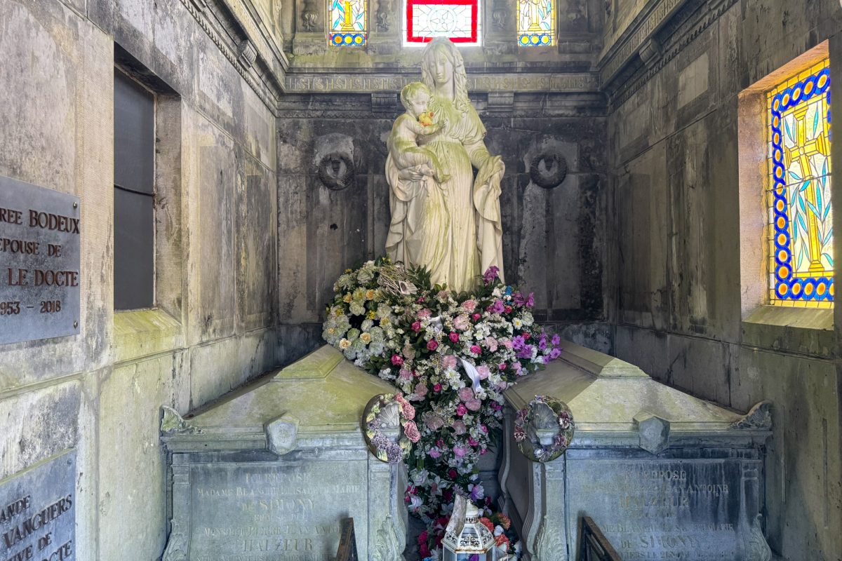 Marienstatue in einem Mausoleum thront über zwei Sarkophagen, davor liegen Blumen