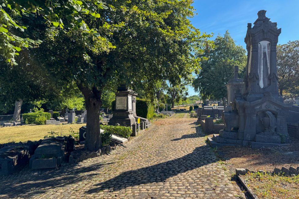 Gräberallee auf dem Friedhof mit vielen Bäumen, rechts ein Mausoleum