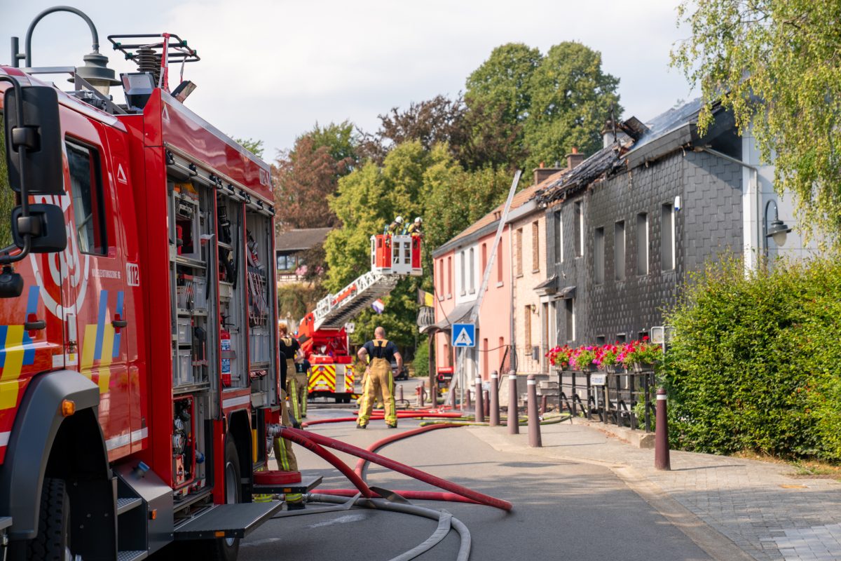 Feuerwehrfahrzeug, Löschschläuche auf der Straße, im Hintergrund Feuerwehrleute