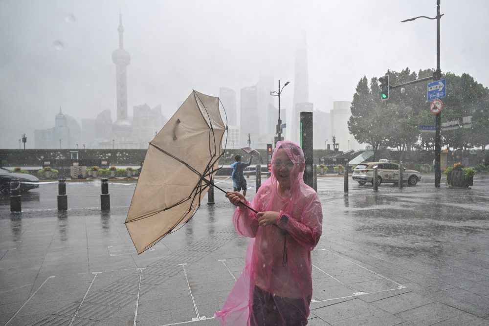 Frau in Regencape hält einen geöffneten und durch den Wind umgeklappten Regenschirm in den Händen