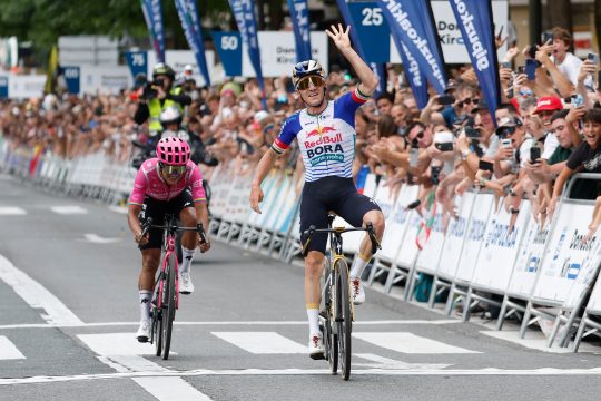 Remco Evenepoel gewinnt zum vierten Mal die Clasica San Sebastian und zeigt vier Finger, links rollt Richard Carapaz ins Ziel