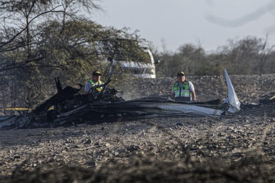 Teile des in Peru abgestürzten Kleinflugzeugs liegen auf dem Boden, zwei Einsatzkräfte stehen dahinter