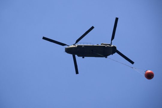 Ein Chinook-Löschhubschrauber der niederländischen Luftwaffe am Himmel, er transportiert Wasser in einem sogenannten "Bambi Bucket"