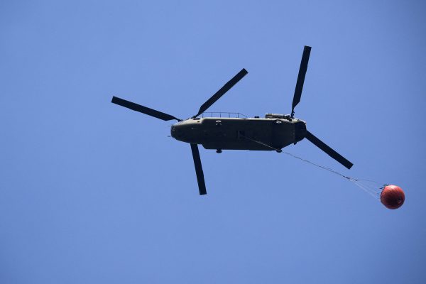 Ein Chinook-Löschhubschrauber der niederländischen Luftwaffe am Himmel, er transportiert Wasser in einem sogenannten "Bambi Bucket"