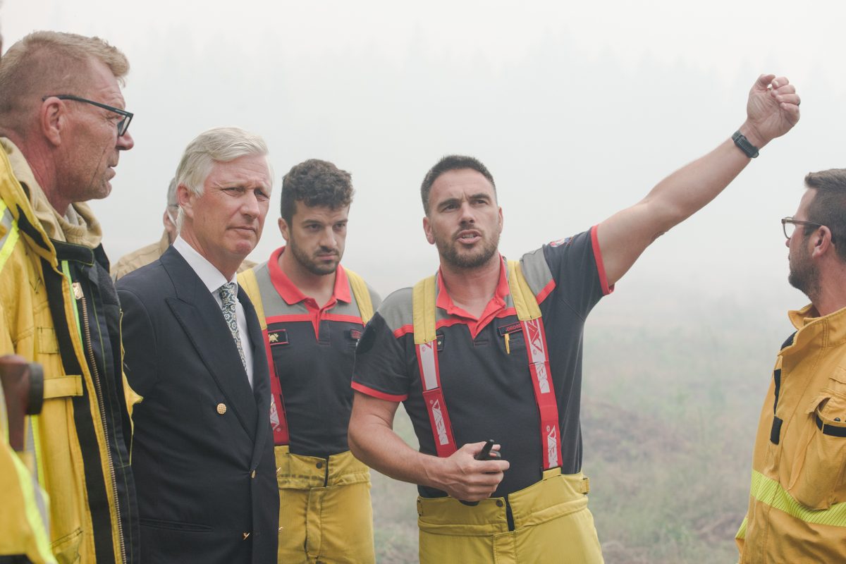 König Philippe hört Rettungskräften zu bei Erklärungen - im Hintergrund dichter Nebel und man erkennt Gestrüpp