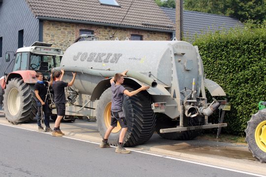 Zwei Landwirte nehmen einen Schlauch ab von einem Anhänger, der offenbar mit Wasser zum Löschen gefüllt ist