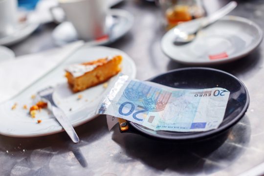 20-Euro-Schein auf einer Untertasse in einem Café, daneben ein Rest Kuchen