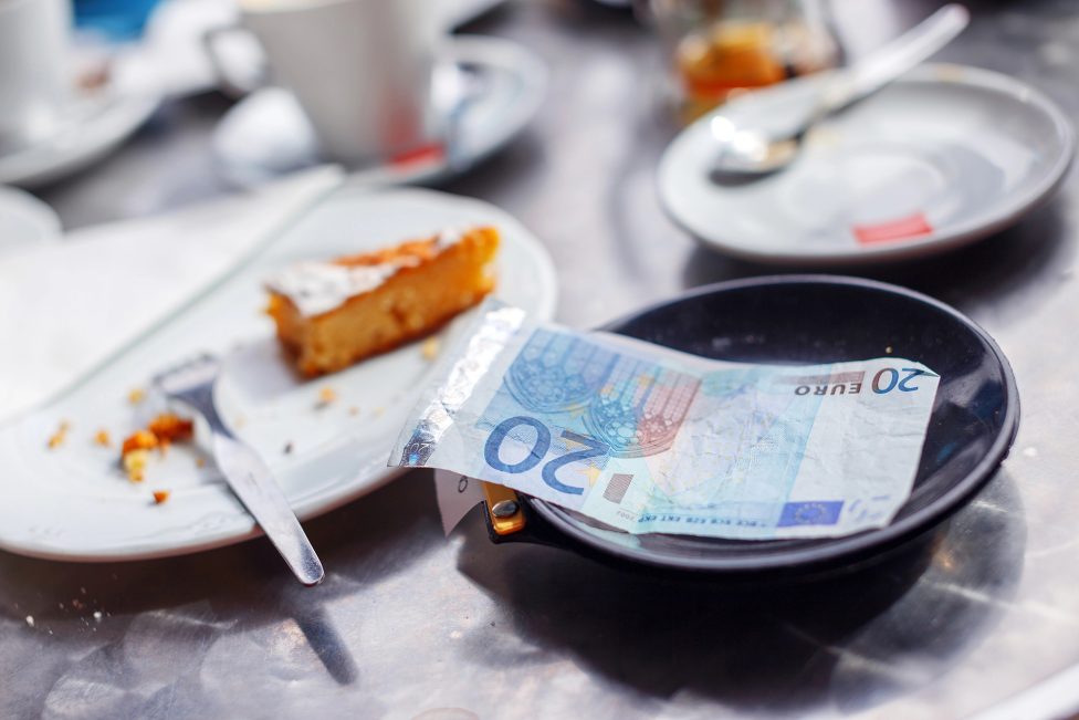20-Euro-Schein auf einer Untertasse in einem Café, daneben ein Rest Kuchen