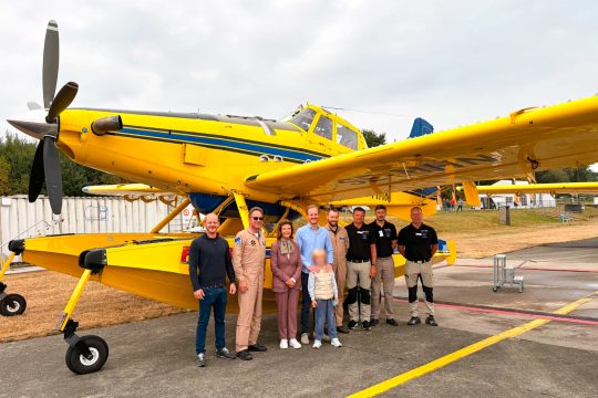 Königin Silvia auf dem Flugplatz von Spa, sie steht mit mehreren Personen direkt neben einem Löschflugzeug