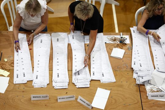 Im Clacton Leisure Centre im Osten Englands zählen Wahlhelfer die Stimmen für die Nachwahl in Clacton aus und stapeln die Wahlzettel auf dem Tisch vor ihnen