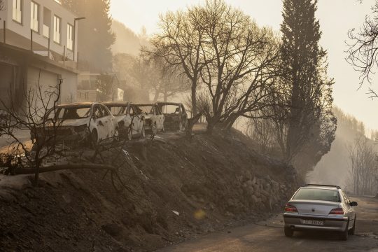 Ein Auto fährt auf einer Straße an ausgebrannten Fahrzeugen vorbei