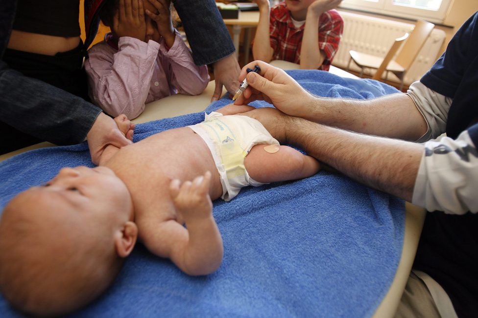 ein Arzt impft ein Baby in den Oberschenkel